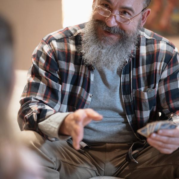 Smiling woman stretching gently on a yoga mat in a sunlit room.
